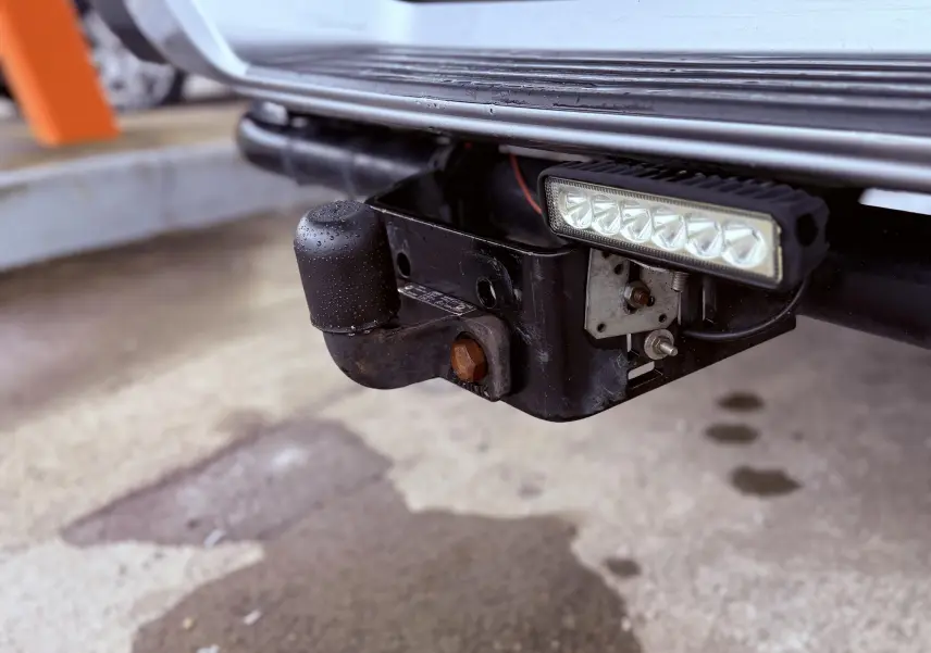 Gros plan sur l'attelage noir et la barre lumineuse LED sous le pare-chocs arrière du Mitsubishi L200 blanc.