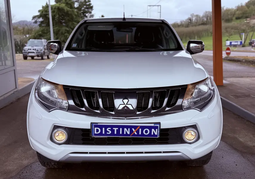 Vue frontale d’un Mitsubishi L200 Club Cab blanc de 2017 avec phares et antibrouillards allumés, calandre noire distinctive.