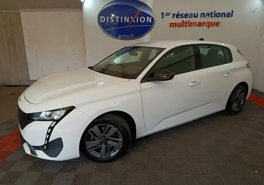 Peugeot 308 blanche vue en 3/4 avant droit, avec phares LED et jantes alliage foncé dans un showroom.