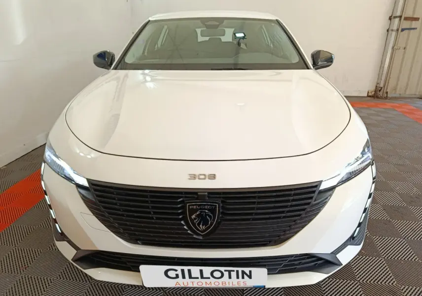 Vue frontale d'une Peugeot 308 blanche 2022 avec calandre noire et feux LED allumés en intérieur.