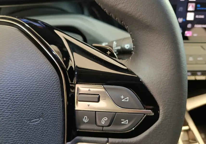 Gros plan sur les commandes multifonctions côté gauche du volant cuir d’une Peugeot 308 blanche, intérieur moderne.