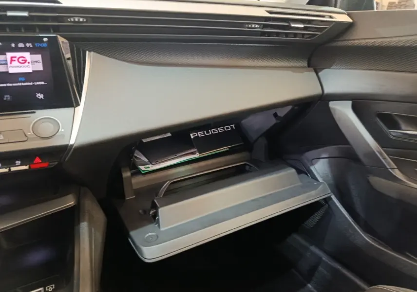 Vue intérieure côté passager de la Peugeot 308 2022, boîte à gants ouverte avec manuel visible, tableau de bord gris.