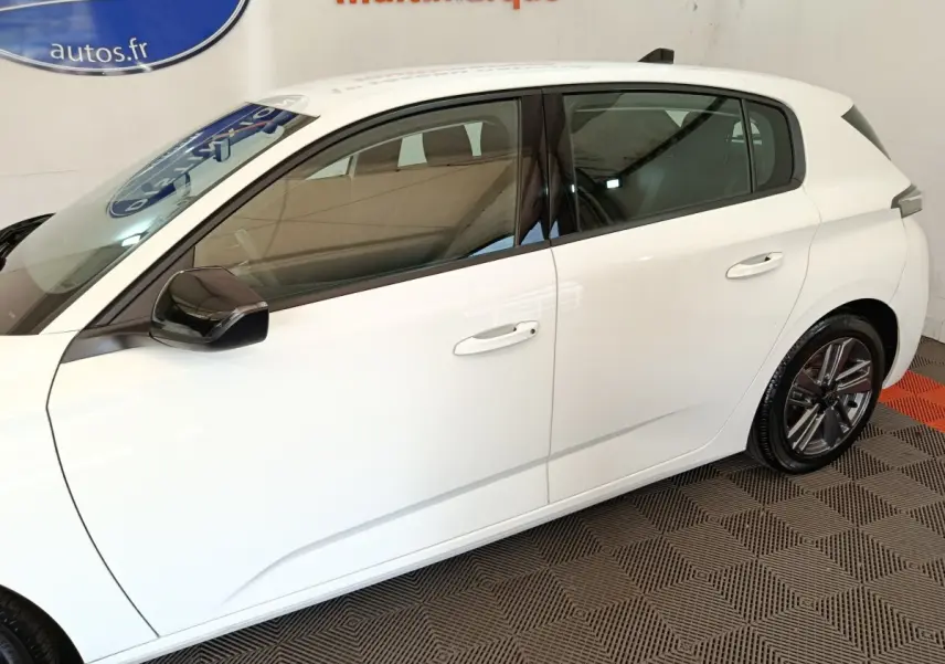 Profil droit d'une Peugeot 308 blanche 2022 avec jantes alliage et rétroviseurs noirs en intérieur showroom.