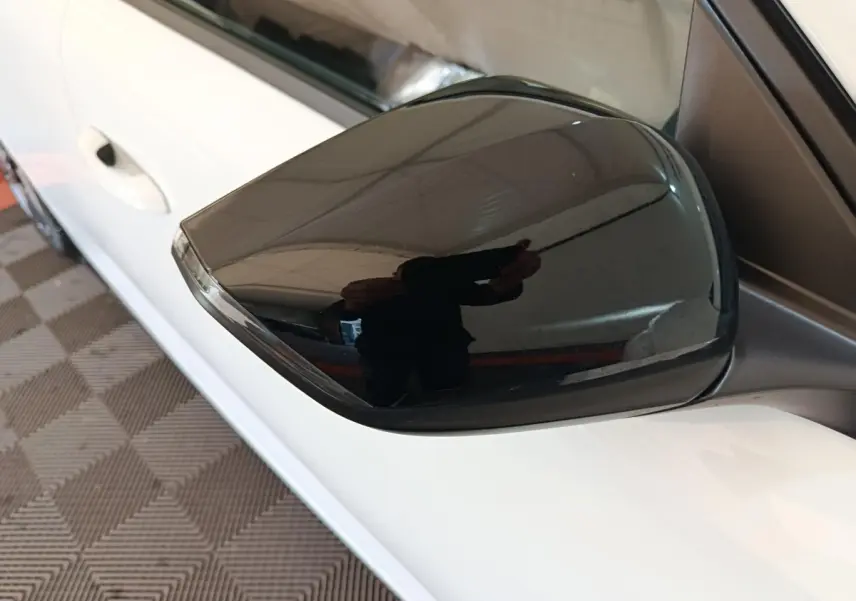 Rétroviseur noir brillant côté conducteur d'une Peugeot 308 blanche vue de près en intérieur.