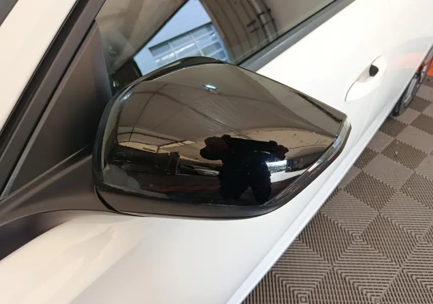 Rétroviseur noir côté conducteur d'une Peugeot 308 blanche vue de près, avec poignée de porte visible.