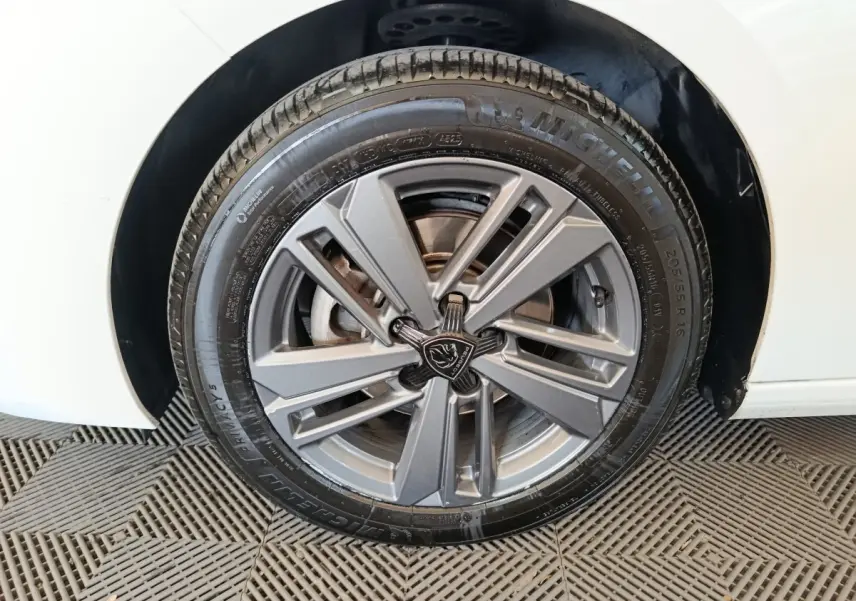 Gros plan sur la roue avant droite d’une Peugeot 308 blanche avec jante alliage gris et logo lion central.