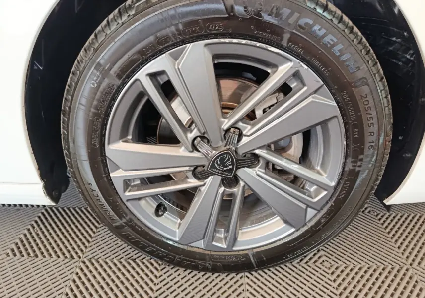 Gros plan sur la roue avant droite d'une Peugeot 308 blanche, mettant en valeur la jante alliage grise au design moderne.