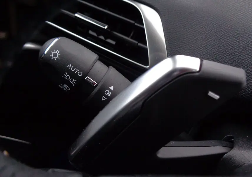 Gros plan sur la commande des phares et la palette de changement de vitesse côté gauche dans l'habitacle noir du Peugeot 3008 2023.