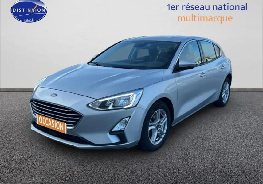 Ford Focus gris clair vue 3/4 avant droit, avec jantes alliage 16 pouces et feux allumés diurnes.