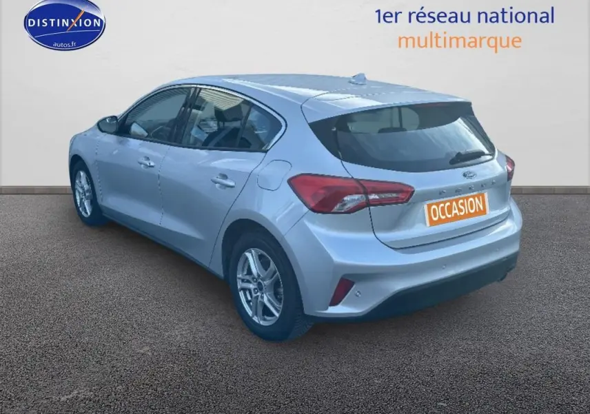Ford Focus gris clair vue 3/4 arrière droit, avec jantes alliage 16 pouces et feux arrière distinctifs.