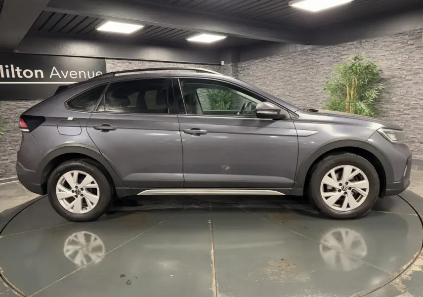 Profil droit d'un Volkswagen Taigo gris 2024 avec jantes alliage Belmopan et lignes fluides sous un éclairage intérieur.