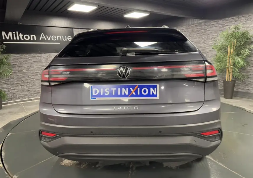 Vue arrière d'un Volkswagen Taigo gris Ascot avec feux arrière LED et logo central lumineux dans un showroom.