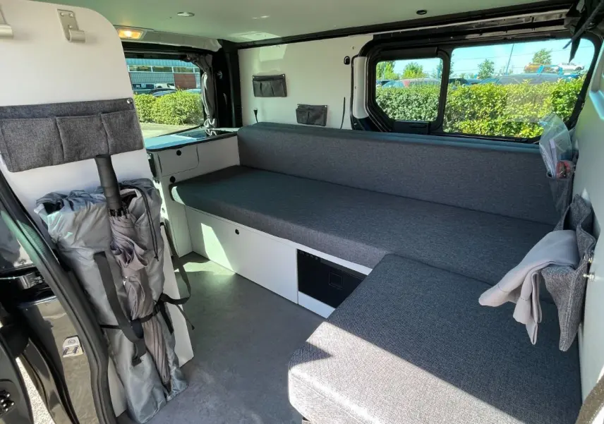Intérieur du Renault Trafic gris comète vu côté droit, montrant banquette et rangements aménagés.