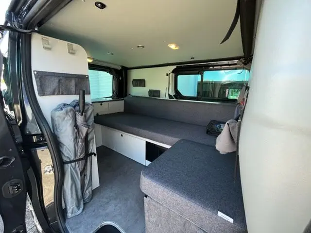Intérieur du Renault Trafic Fourgon gris Comète, vue latérale droite montrant banquettes convertibles et rangements intégrés.