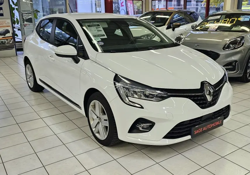 Renault Clio blanc glacier vue 3/4 avant droit en showroom, avec phares LED et calandre noire distinctive.