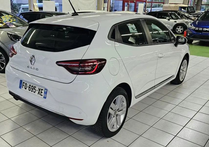 Vue 3/4 arrière droite d'une Renault Clio blanche Glacier en showroom avec jantes alliage et feux LED distinctifs.