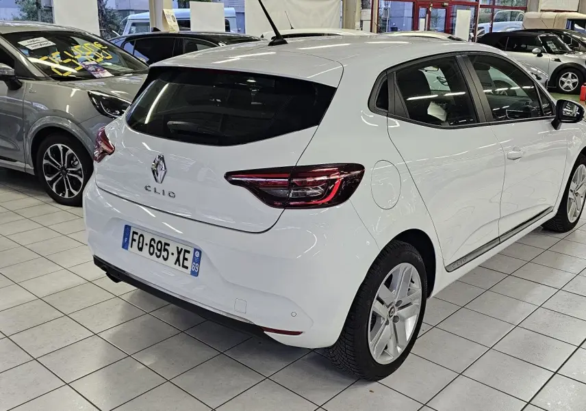 Renault Clio blanc glacier vue 3/4 arrière droit dans un showroom, avec feux arrière LED distinctifs.