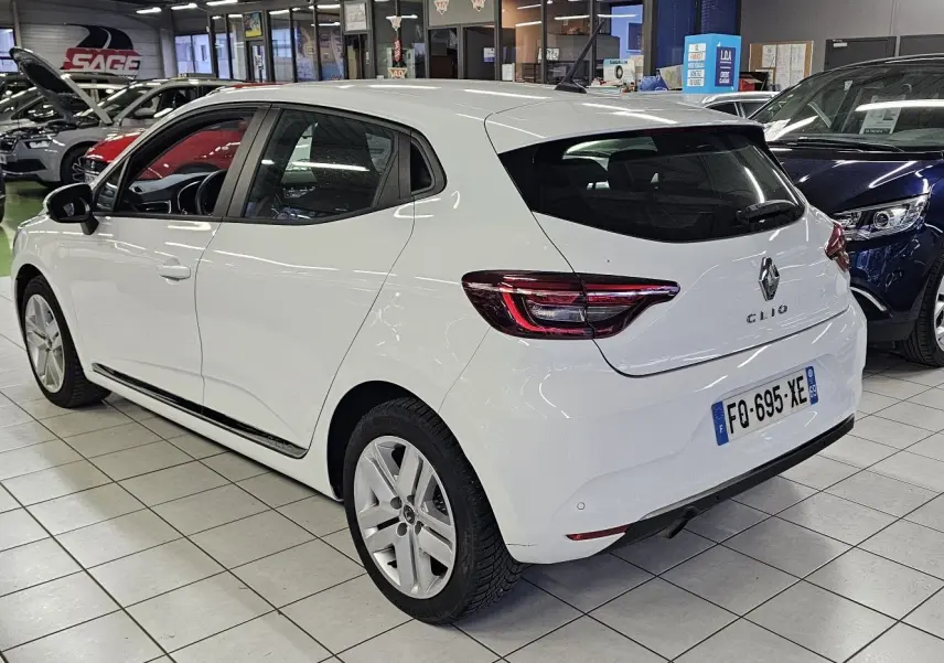 Vue 3/4 arrière droite d'une Renault Clio blanche Glacier 2020 en intérieur, avec feux arrière LED et cinq portes visibles.