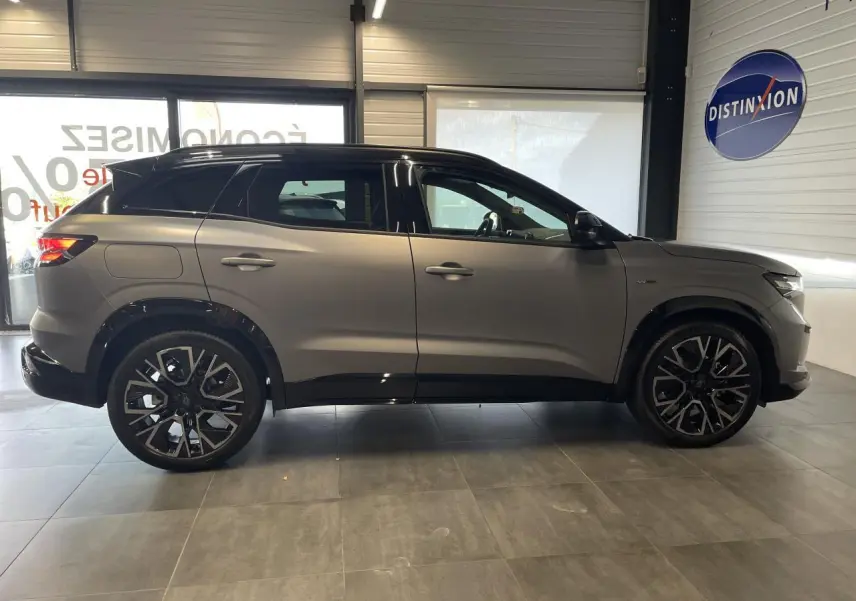 Profil côté gauche du Renault Austral gris satin mat avec toit noir et jantes alliage noires en showroom.