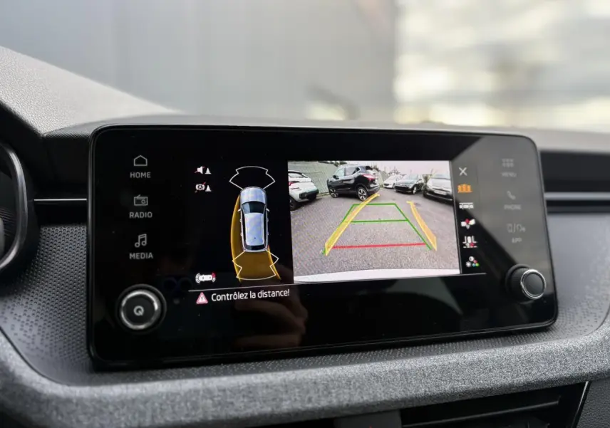 Écran central du Skoda Kamiq TSI 116 DSG7 montrant la caméra de recul et l'aide au stationnement en marche.
