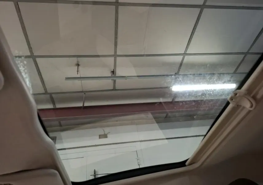 Vue intérieure du toit ouvrant panoramique d'une Fiat 500 Dolcevita gris électroclash, éclairage de garage visible.