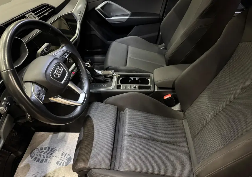 Vue intérieure côté conducteur de l'Audi Q3 Business 2019 avec sellerie tissu gris et volant multifonction.