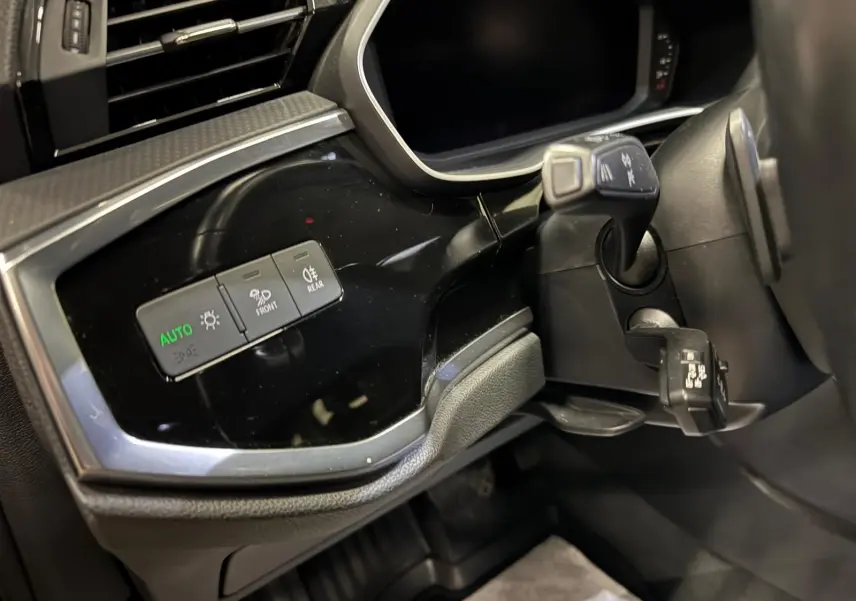 Détail du tableau de bord côté gauche de l'Audi Q3 Business gris, avec commandes d'éclairage et inserts noir brillant.