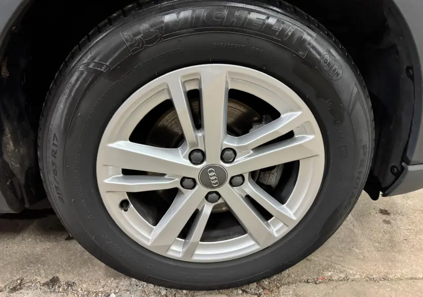 Gros plan sur la jante alliage argentée avec logo Audi d’un Audi Q3 Business gris, pneu Michelin visible.