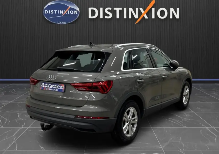 Vue 3/4 arrière droite d'un Audi Q3 Business gris avec feux arrière LED dynamiques et attelage visible en intérieur showroom.