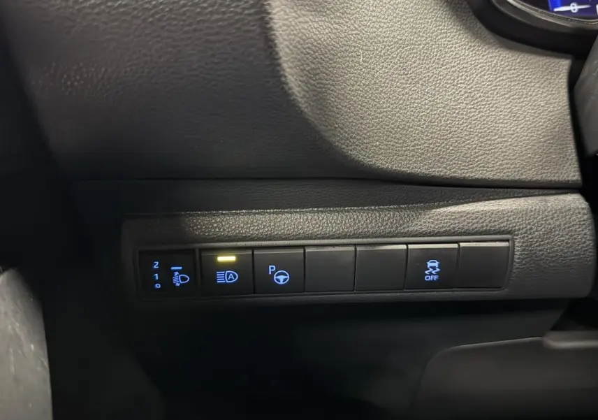 Gros plan sur les commandes de bord noires éclairées en bleu et jaune dans l'habitacle de la Toyota Corolla hybride gris 2022.