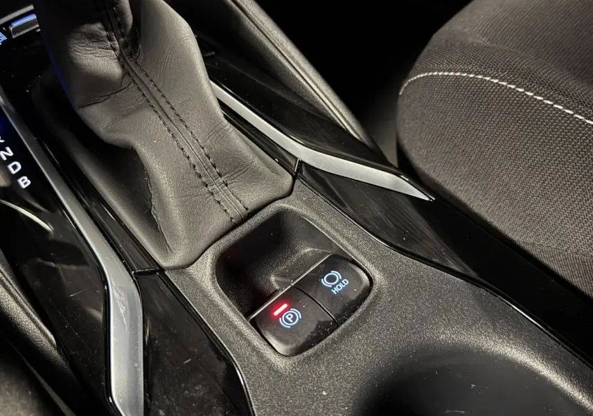 Gros plan sur la console centrale noire laquée de la Toyota Corolla hybride 2022 avec levier de vitesses cuir et frein électrique.