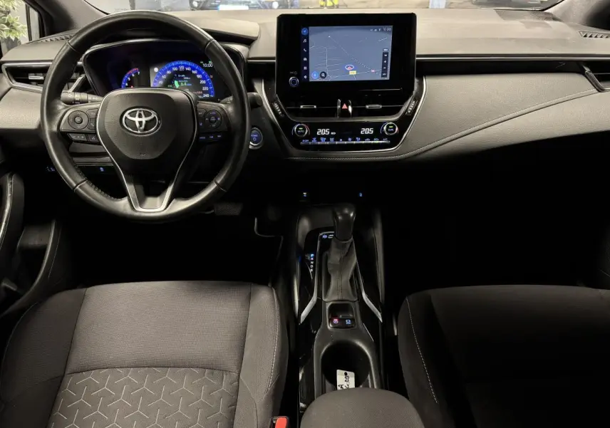 Intérieur de la Toyota Corolla Hybride 2022 vu de face, tableau de bord noir avec écran tactile et volant cuir multifonction.