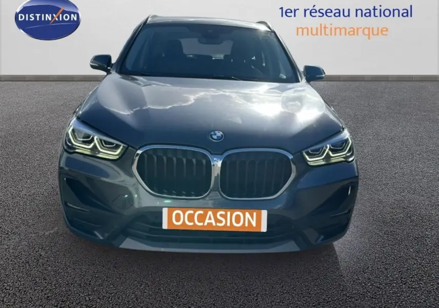 BMW X1 gris foncé vue de face avec calandre double et phares LED allumés sur fond neutre.