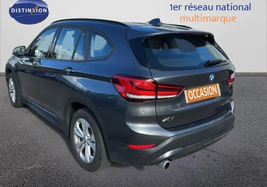 Vue 3/4 arrière droite d'un BMW X1 gris foncé avec jantes alliage et vitres surteintées, en extérieur sur sol bitumé.