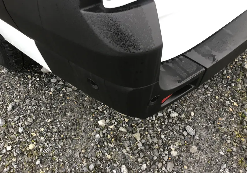 Gros plan sur l'angle arrière droit du pare-chocs noir d'un Renault Master blanc, avec capteurs de recul visibles.