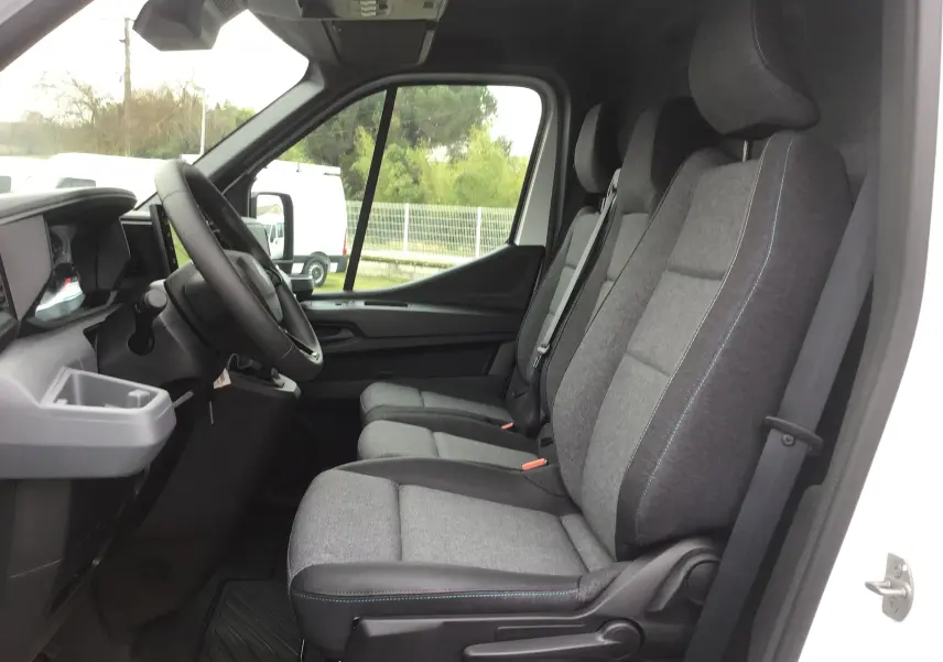 Vue intérieure côté conducteur du Renault Master blanc 2025, montrant les trois sièges avant gris avec coutures bleues et tableau de bord.