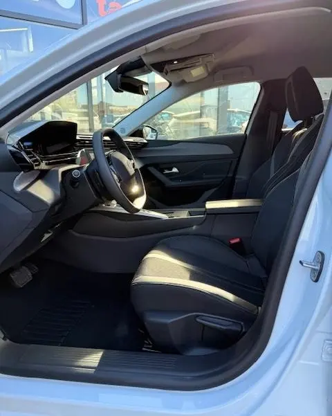 Vue intérieure côté conducteur de la Peugeot 308 Hybrid blanche 2025, avec tableau de bord numérique et sièges noirs.