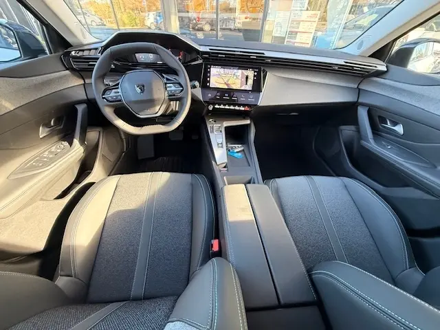 Vue intérieure avant de la Peugeot 308 Hybrid blanche 2025, tableau de bord moderne avec écran tactile central et volant cuir multifonctions.