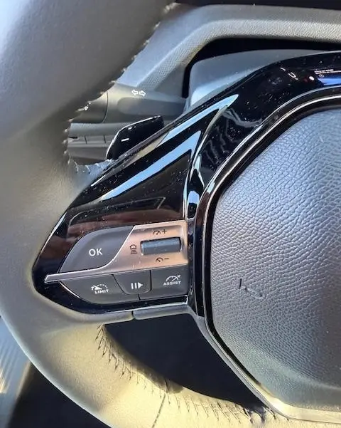 Gros plan sur les commandes multifonctions côté gauche du volant cuir de la Peugeot 308 Hybrid 145 e-DCS6 Allure 2025.
