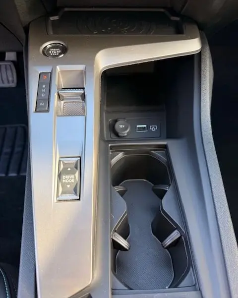 Vue rapprochée de la console centrale grise de la Peugeot 308 Hybrid 145 e-DCS6 Allure avec boutons de sélection et porte-gobelets.