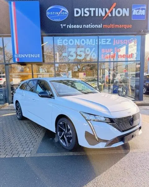 Peugeot 308 Hybrid blanc vue 3/4 avant droit, calandre noire distinctive et phares LED verticaux, devant concession multimarque.