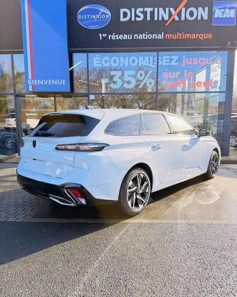 Vue 3/4 arrière droite d'une Peugeot 308 Hybrid 145 e-DCS6 Allure blanche garée devant un concessionnaire multimarque.