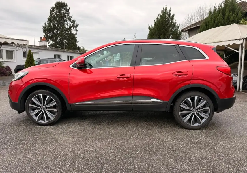 Vue de profil côté gauche d'un Renault Kadjar rouge flamme avec jantes alliage bicolores et protections noires basses.
