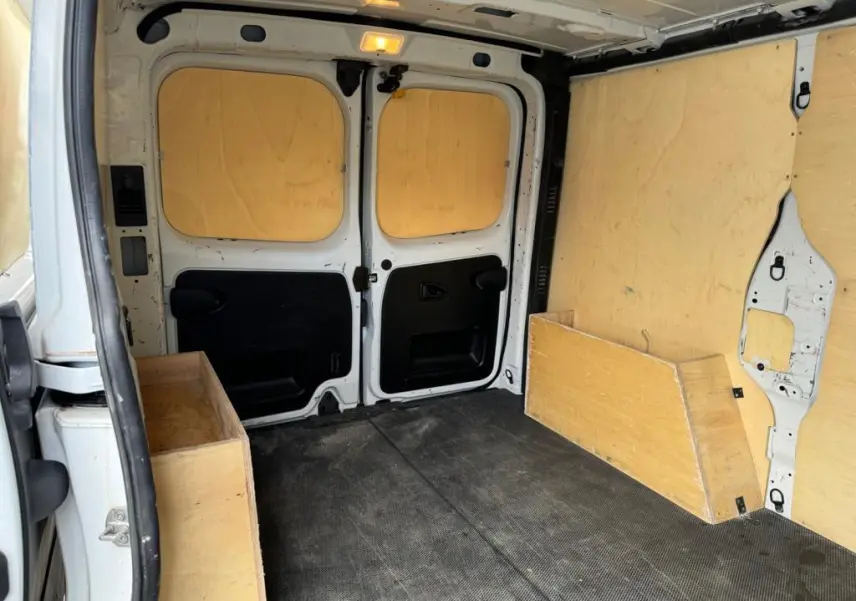 Intérieur du coffre du Nissan Primastar blanc, vue arrière avec plancher et protections latérales en bois.