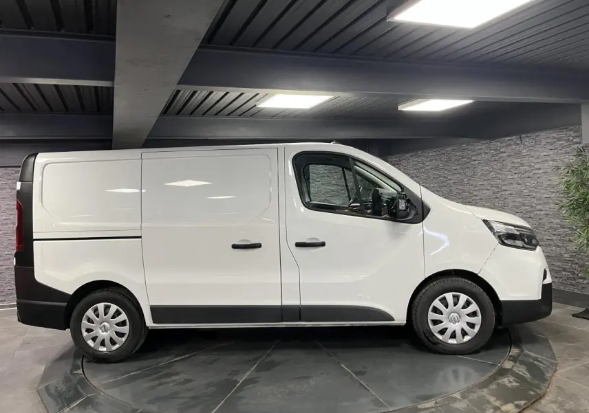 Vue de profil côté droit d'un utilitaire Nissan Primastar blanc avec enjoliveurs de roues et protections noires.