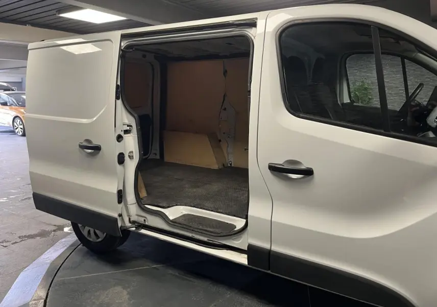 Vue latérale droite d'un Nissan Primastar blanc avec porte coulissante ouverte montrant l'espace de chargement bois.