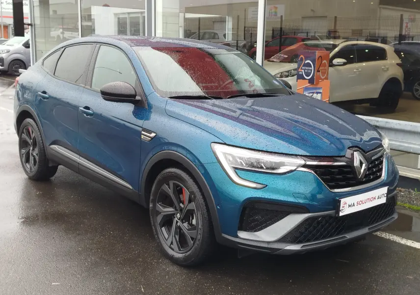 Vue 3/4 avant gauche d'un Renault Arkana 1.6 E-Tech bleu Zanzibar, avec jantes noires et détails rouges sous la pluie.