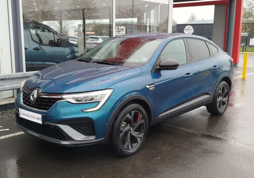 Renault Arkana 1.6 E-Tech bleu Zanzibar en 3/4 avant droit, avec jantes noires et détails rouges sous la pluie.