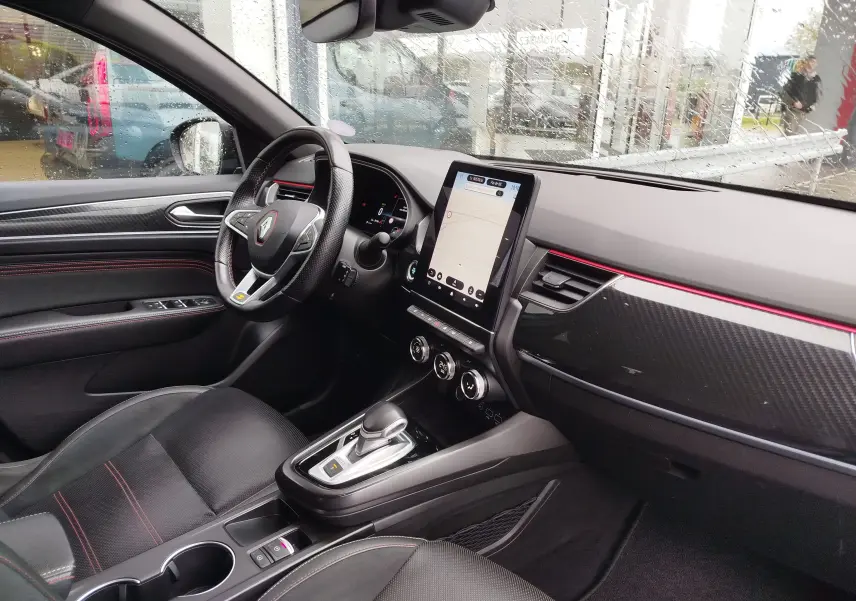 Vue intérieure côté conducteur du Renault Arkana 1.6 E-Tech bleu Zanzibar, avec tableau de bord noir et écran tactile vertical.