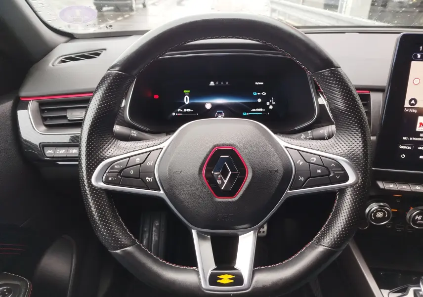 Vue intérieure centrée sur le volant noir perforé avec surpiqûres rouges du Renault Arkana bleu Zanzibar, tableau de bord digital visible.